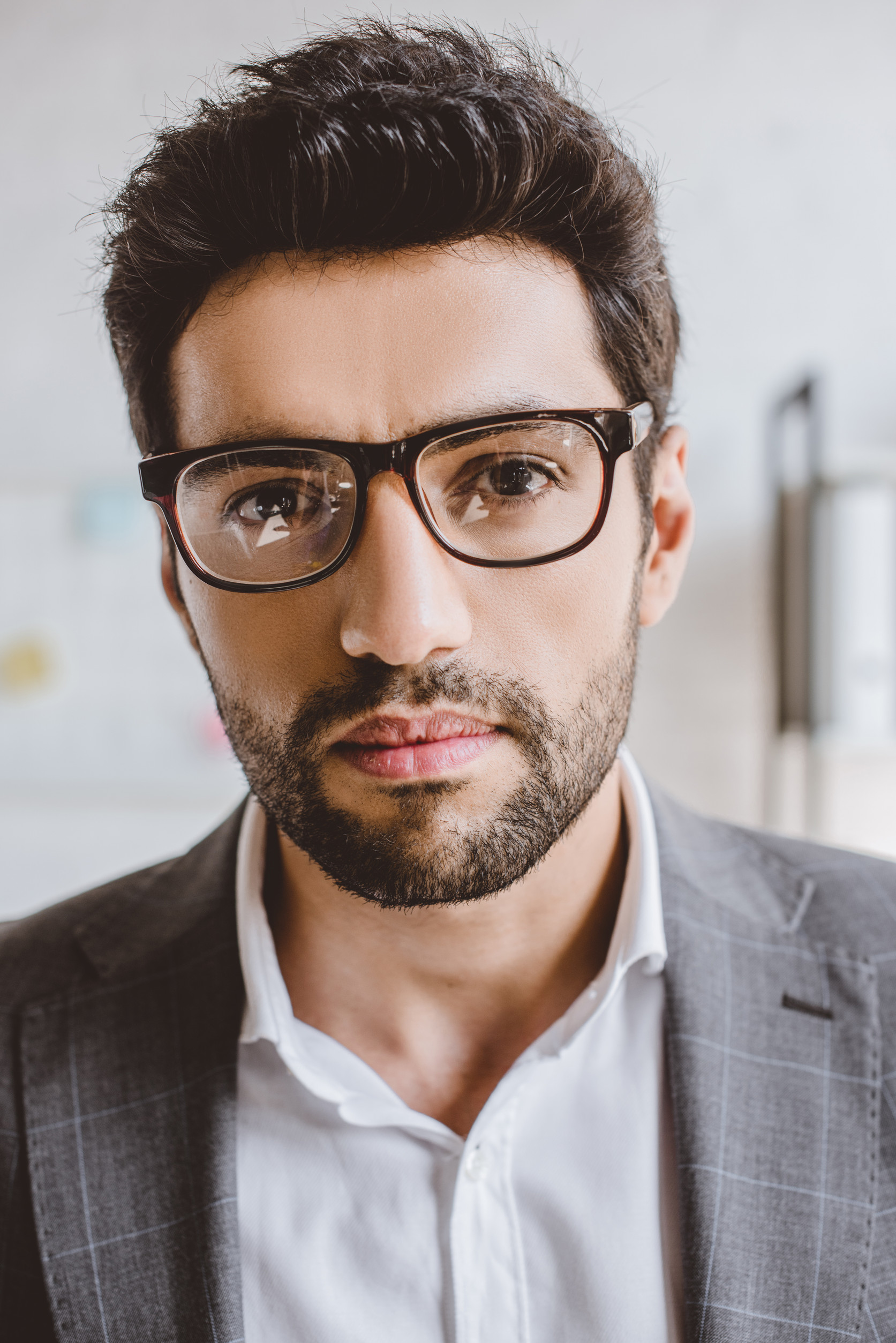 portrait of handsome businessman with bristle in glasses looking at camera in office